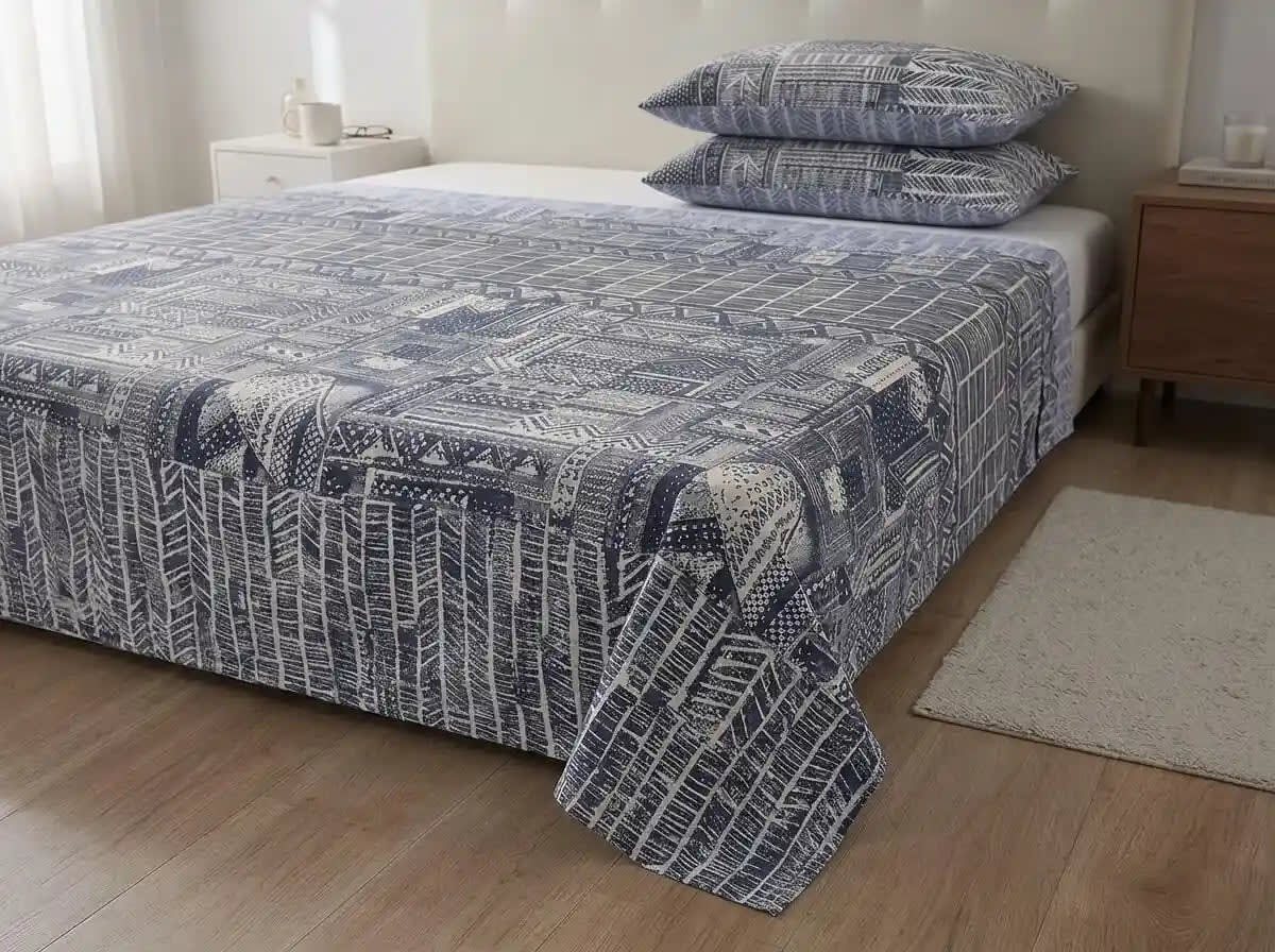 A bed dressed in a blue and white geometric patterned quilt or comforter set with matching pillows, shown in a styled bedroom with wood flooring, bedside tables, and a rug.