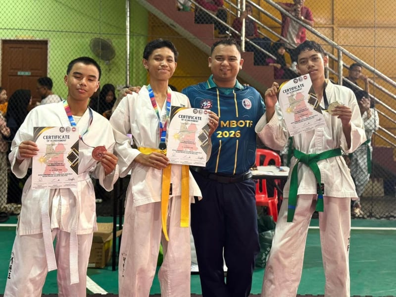 Tiga pelajar berpakaian taekwondo putih menunjukkan sijil dan pingat, bersama seorang lelaki berbaju MBOTF 2026