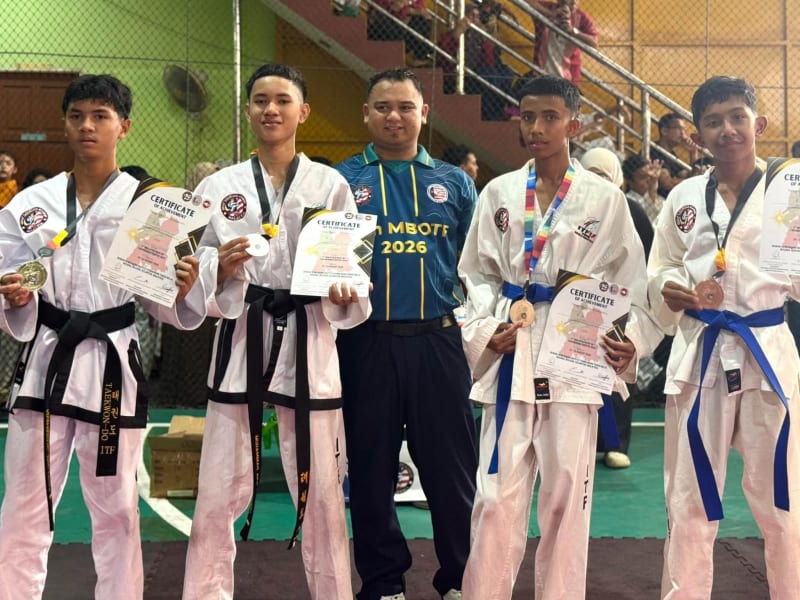 Empat pelajar bertali pinggang hitam dan biru memegang pingat dan sijil, dengan seorang lelaki berbaju MBOTF 2026 di tengah