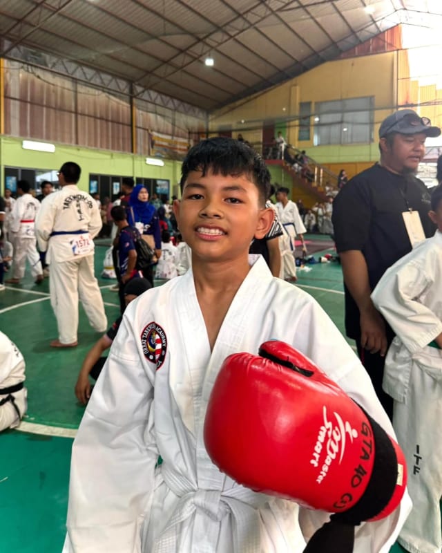 Seorang pelajar tersenyum dengan sarung tangan sparring merah di dewan kejohanan