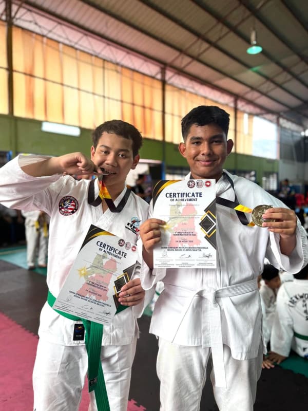 Dua pelajar bergambar dengan sijil pencapaian dan pingat; seorang daripadanya menggigit pingat