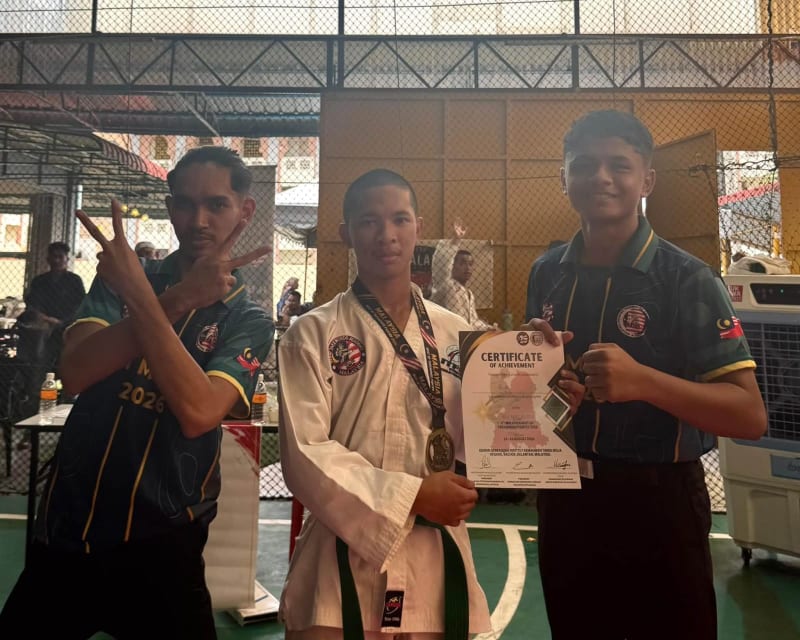 Seorang pelajar berpakaian taekwondo memegang pingat dan sijil, diapit dua rakan berjersi pasukan