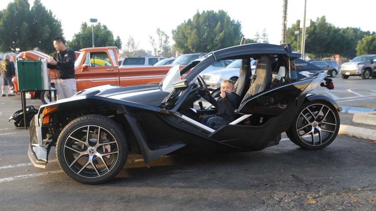 a little kid smiling in the front seat of the Polaris Slingshot at Carcadia car meet.