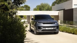 Silver-gray 2023 Range Rover Sport Dynamic SE P400 in front three-quarter view outside a modern stone building.