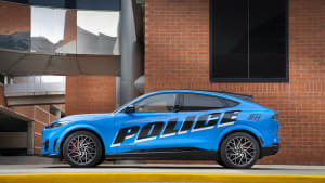 a blue Ford Mach E police car on the street, with a brick building in the background.
