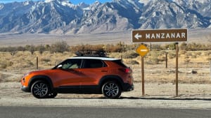 an orange 2022 Chevrolet Trailblazer on a desert highway with snow-capped mountains in the background and a sign pointing to Manzanar in the foreground.