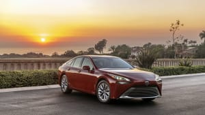 A red 2021 Toyota Mirai on a cliffside road with the sun setting in the background.