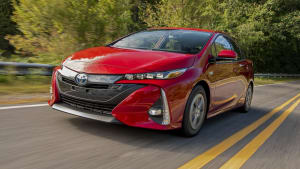 a red Toyota Prius Prime, traveling towards the camera, on an American highway. 