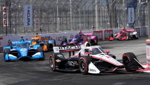 Josef Newgarden coming around a corder with a row of race cars behind him.