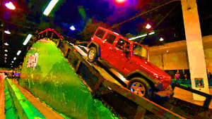 Image of a red Jeep Wrangler going over a homemade mountain course at a car show.