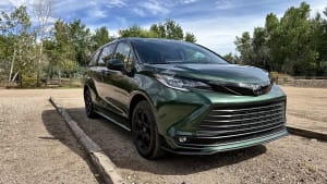 Dark green 2026 Toyota Sienna Woodland Edition photographed from the front three-quarter angle, with black wheels in a wooded parking area.