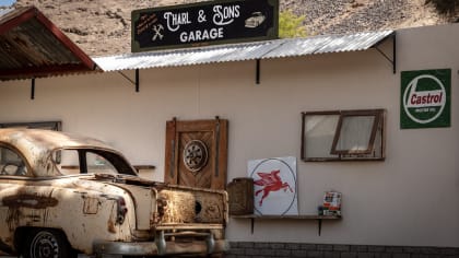 a garage sign on the roof of a rustic workshop, with a rusty car in the foreground.