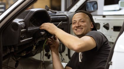 car mechanic working with wires inside a stripped vehicle.