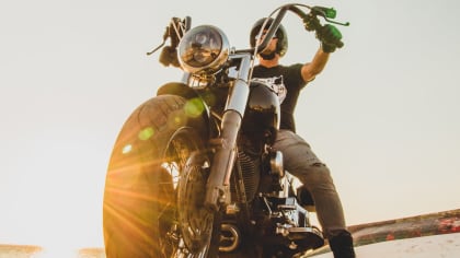 closeup of a motorcycle with a person on it and the sun setting in the background