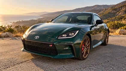 Digitally altered front three-quarter image of a dark green 2025 Toyota GR86 with bronze wheels at a generated coastal overlook.