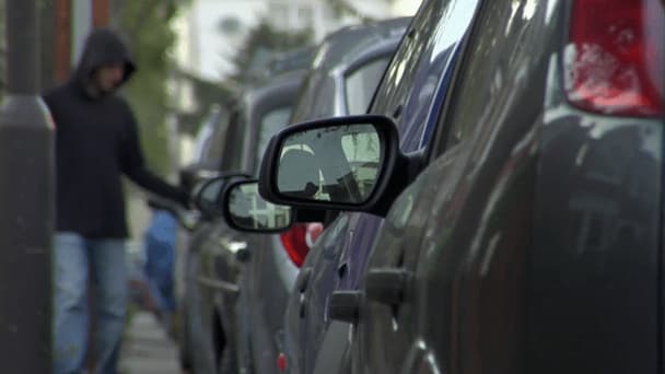 a man is walking past parked cars, checking if the vehicle is unlocked. Image from a NCIB video.