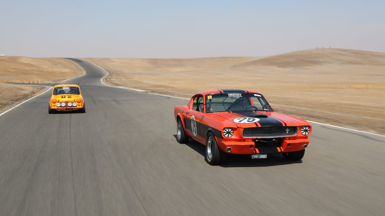 two vintage race cars coming at your on a race track in the desert.