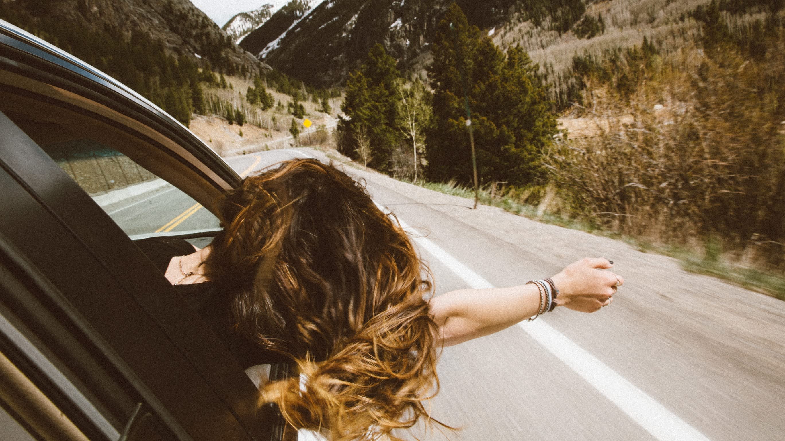 woman with hand out of the car while driving through a canyon
