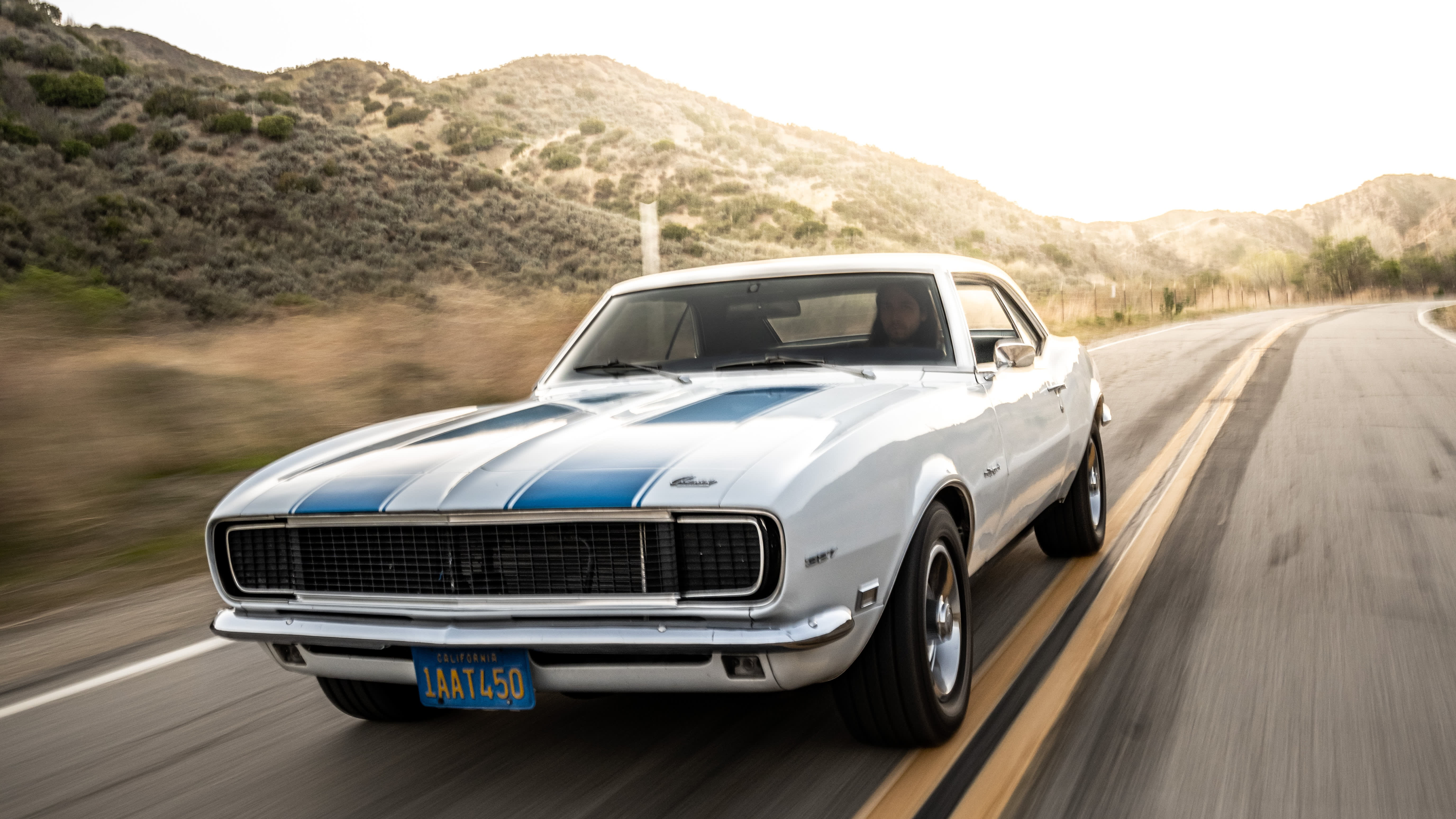 classic white Camaro driving down road during daytime.