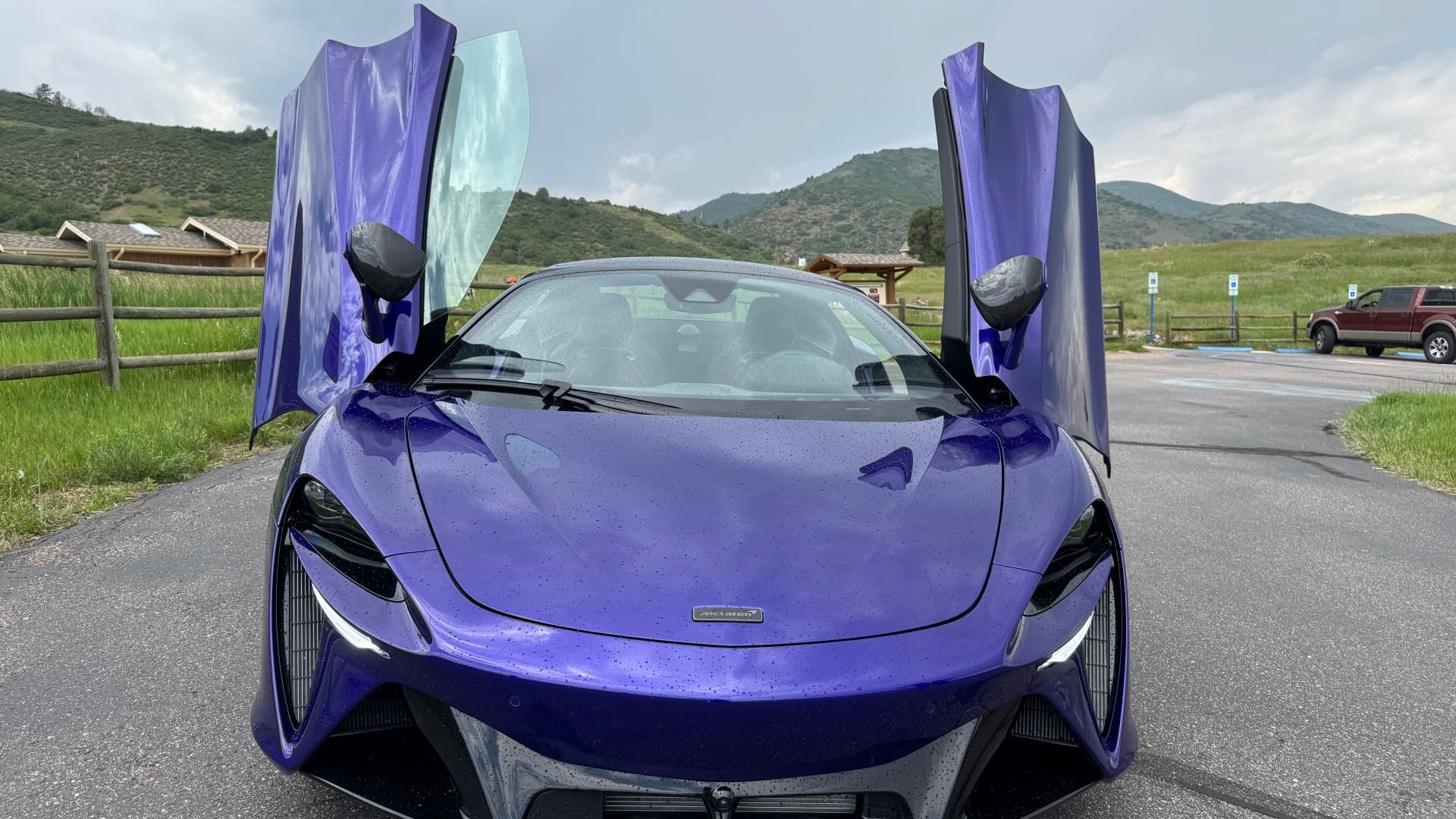 a blue mclaren artura with both doors open, seen from the front