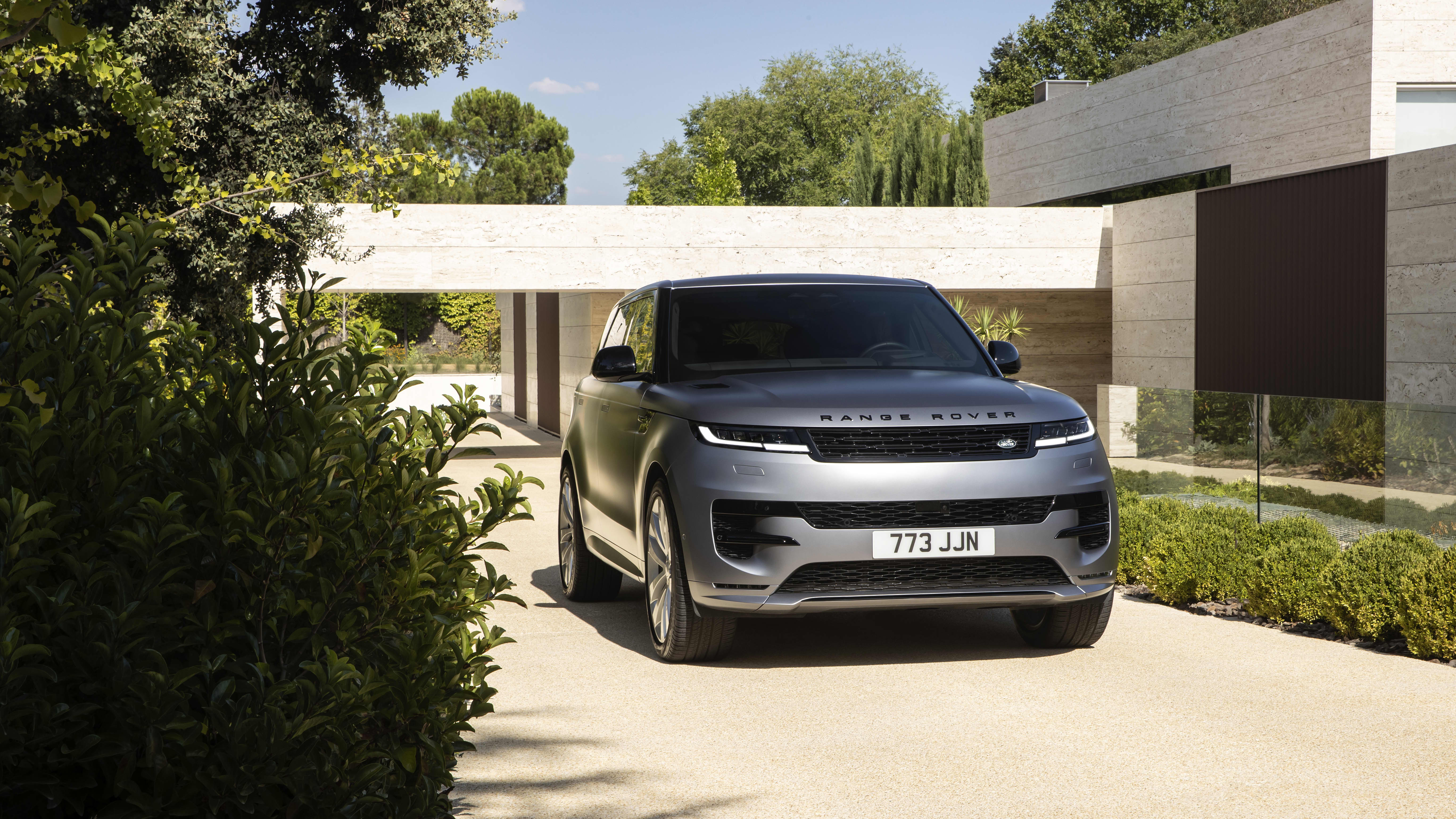 Silver-gray 2023 Range Rover Sport Dynamic SE P400 in front three-quarter view outside a modern stone building.