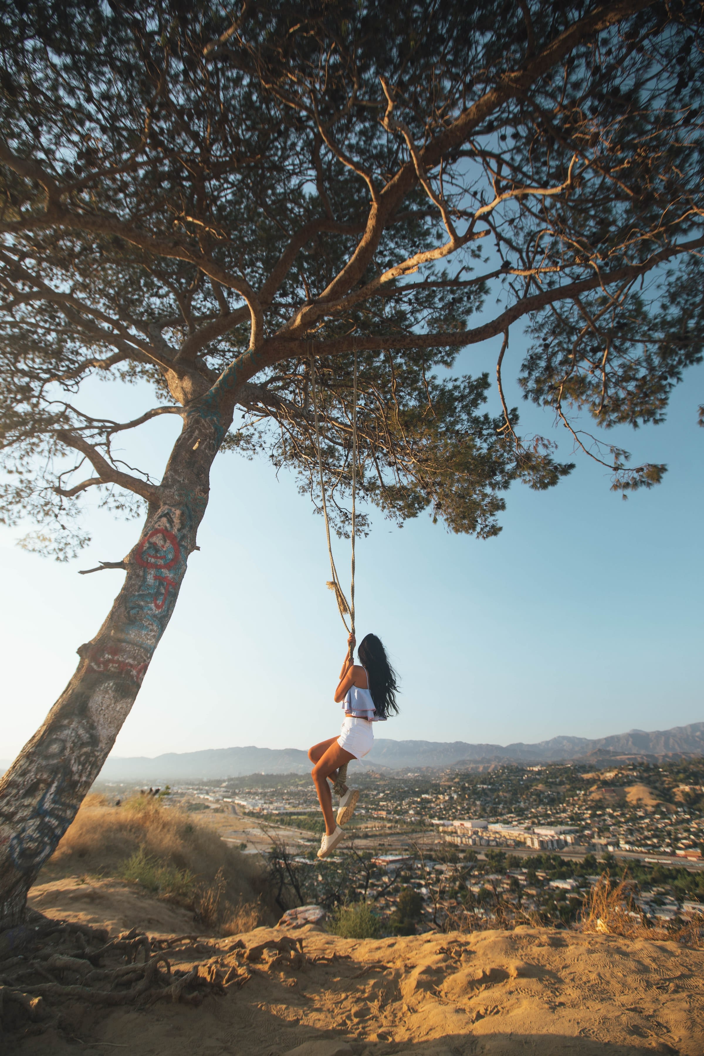 Woman swinging from the Secret Swing in Elysian Park, the dry landscape of rural Los Angeles spreads out below.