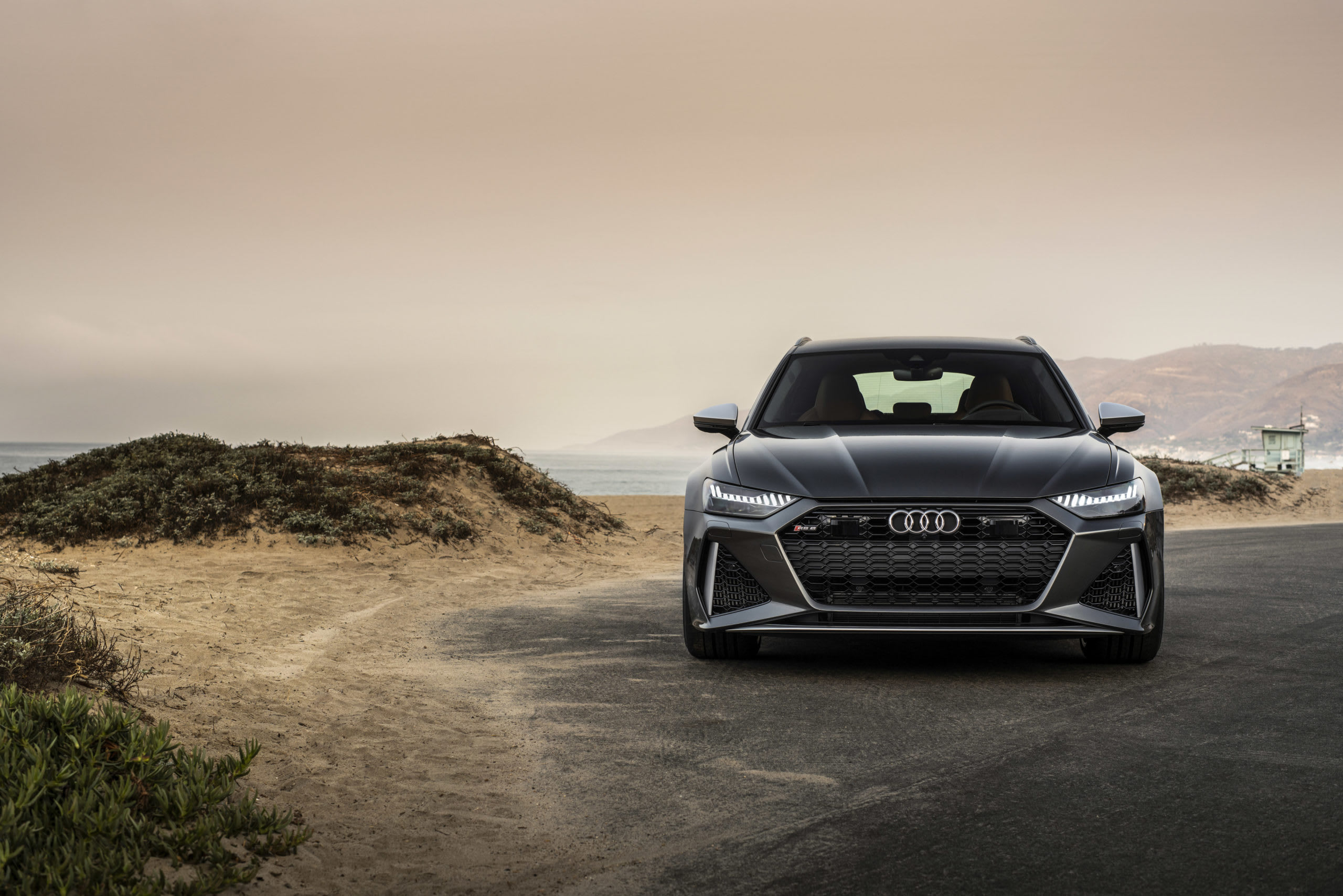 a grey Audi RS6 avant station wagon on a cliff-side road at the beach with the ocean in the background.