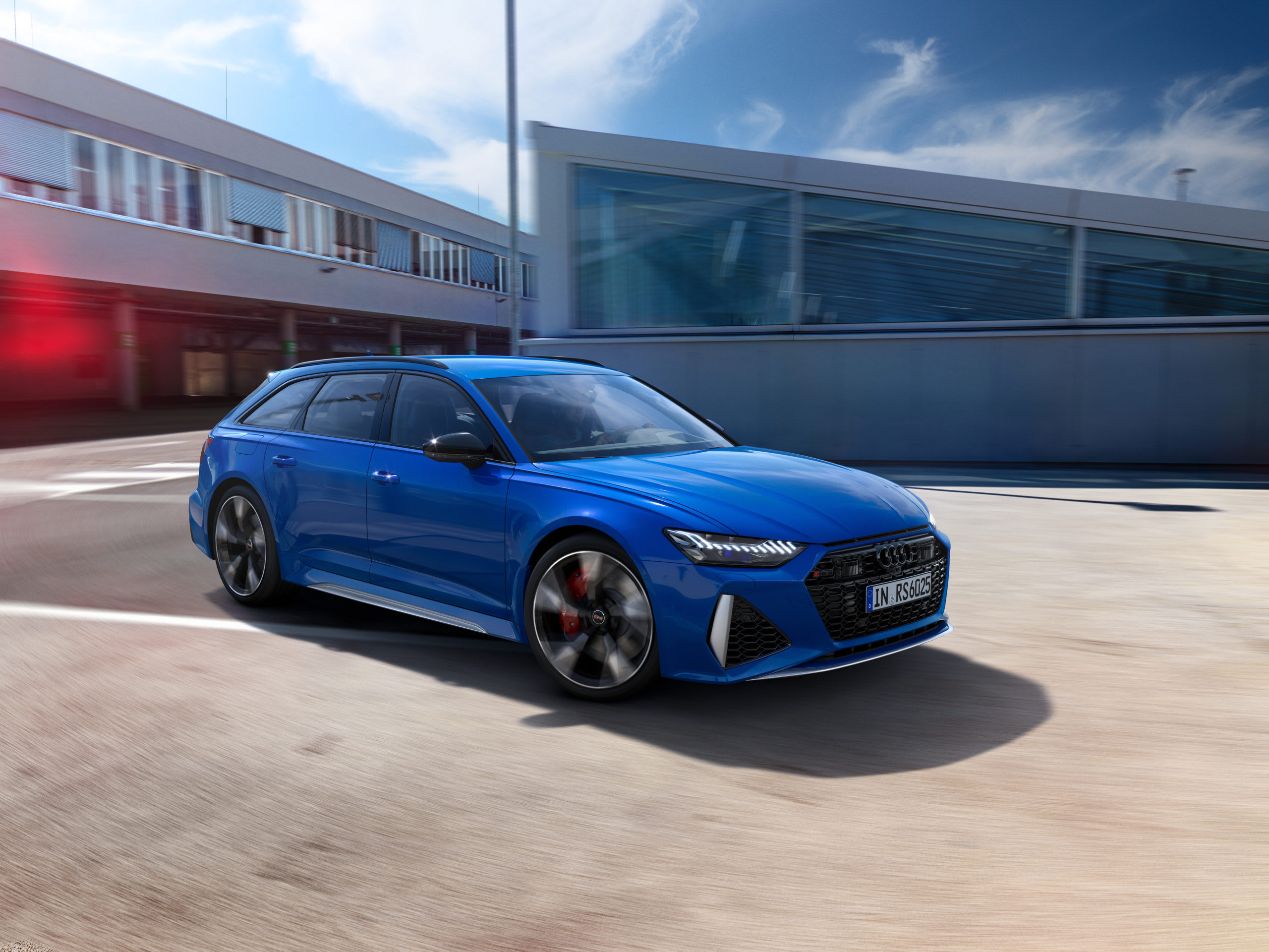 a blue Audi RS6 avant station wagon cruising through a hip part of town.