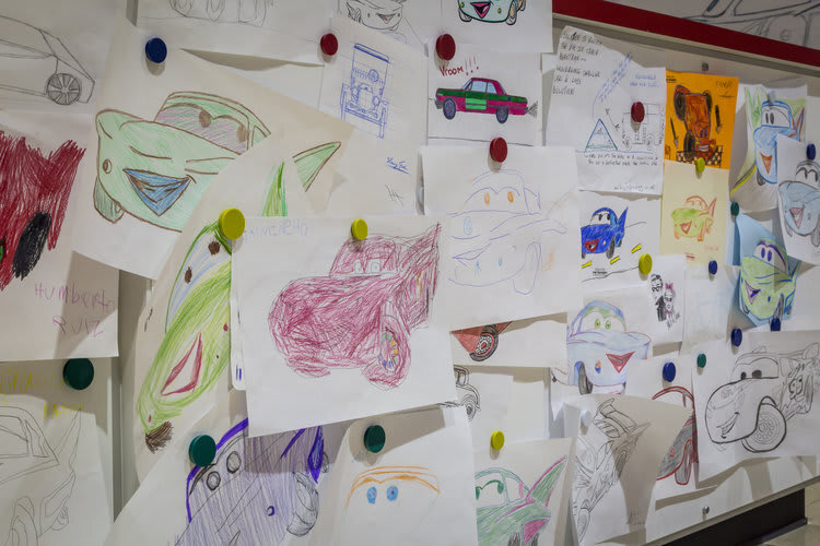 children's drawings hanging on a wall - featuring cars of all sorts and sizes.