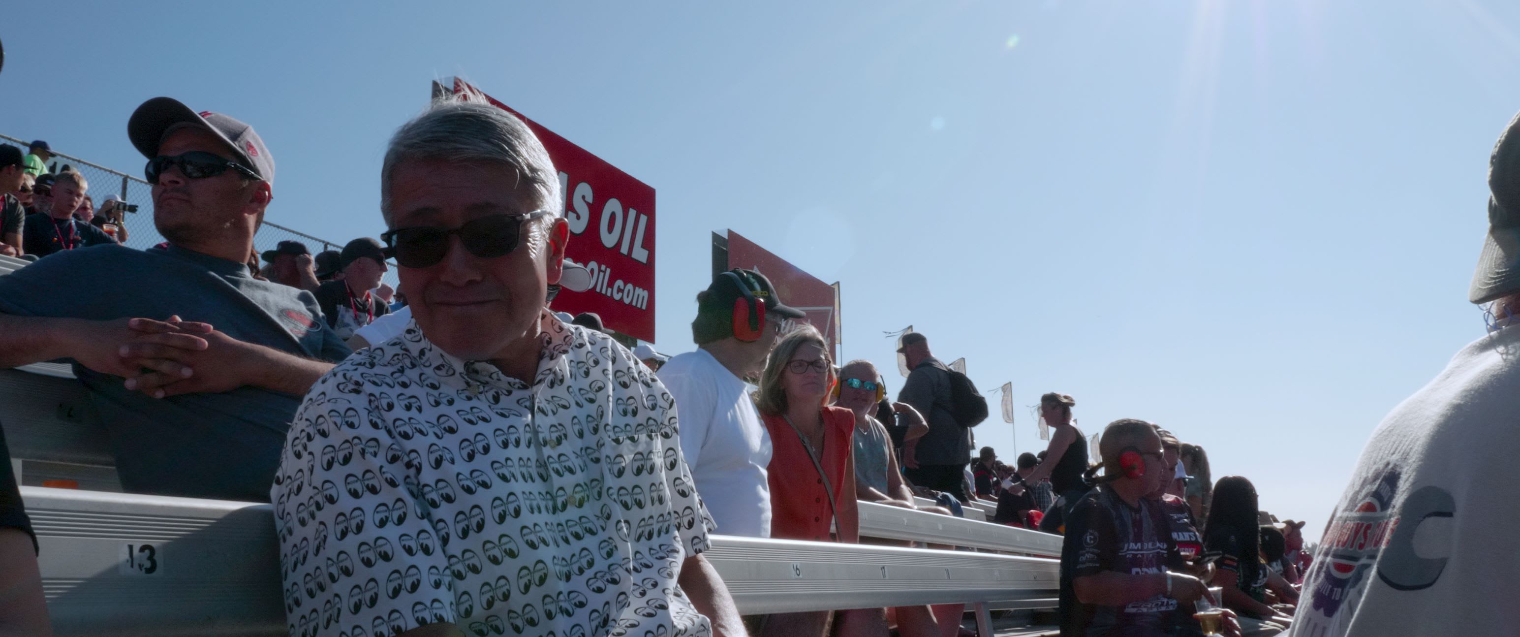 Owner of Mooneyes Shige Suganuma sitting in the bleachers of a drag race