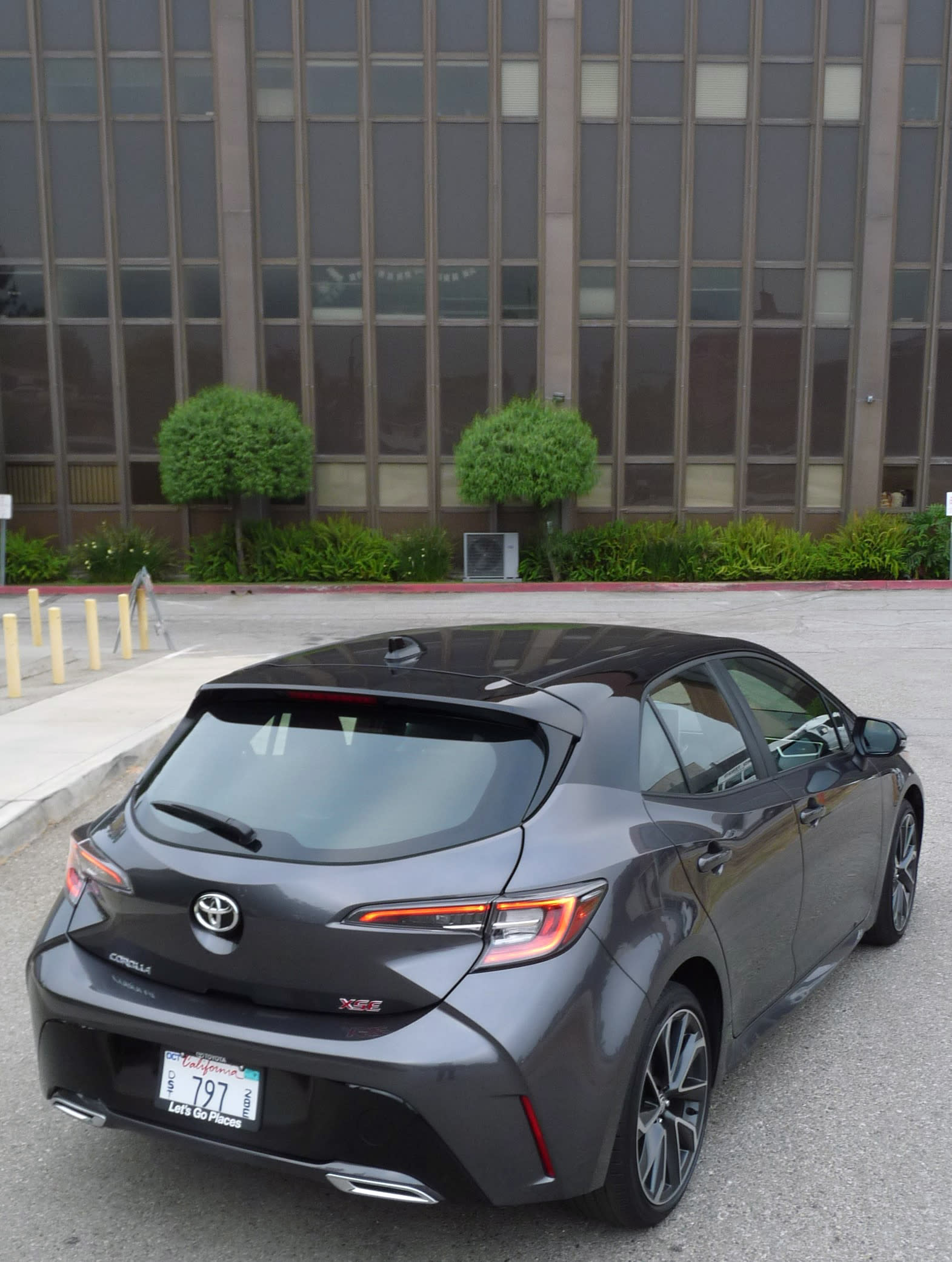 image taken a little from above of a 2021 Toyota Carolla Hatchback - gray with a black roof - with an office building in the background.