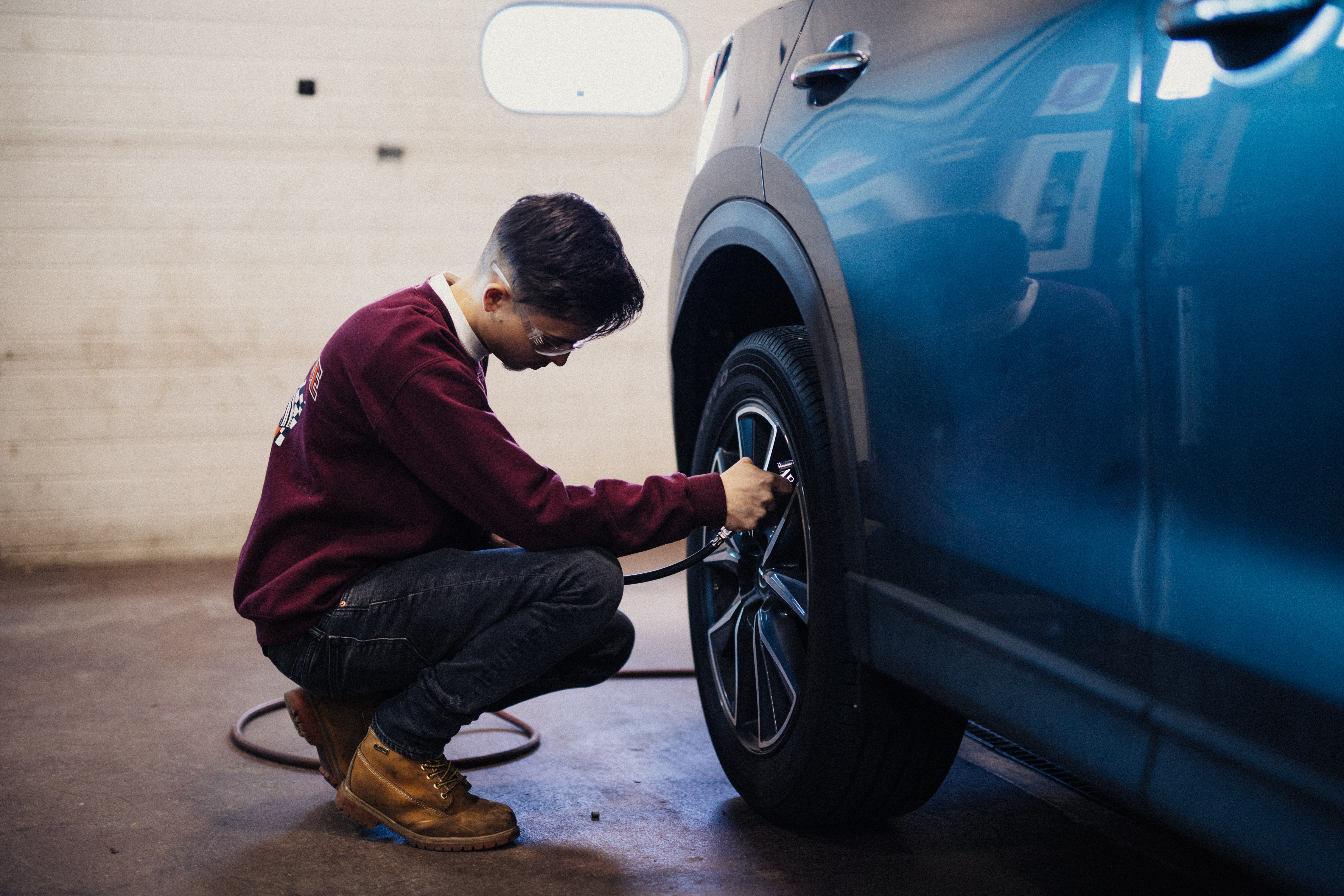 student checking the tire pressure in blue car.