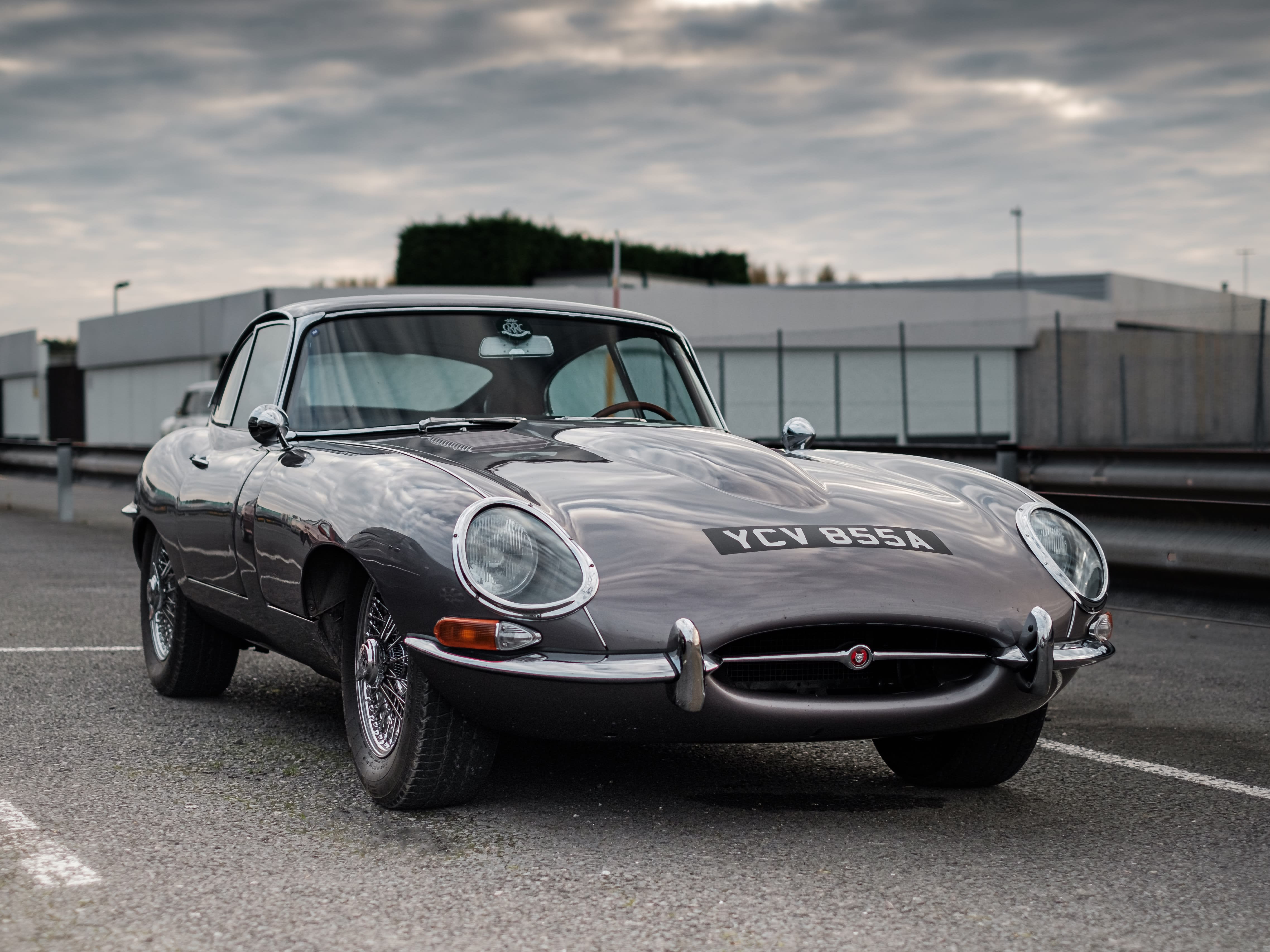 Grey Jaguar on what looks like a racetrack, with some buildings in the background.