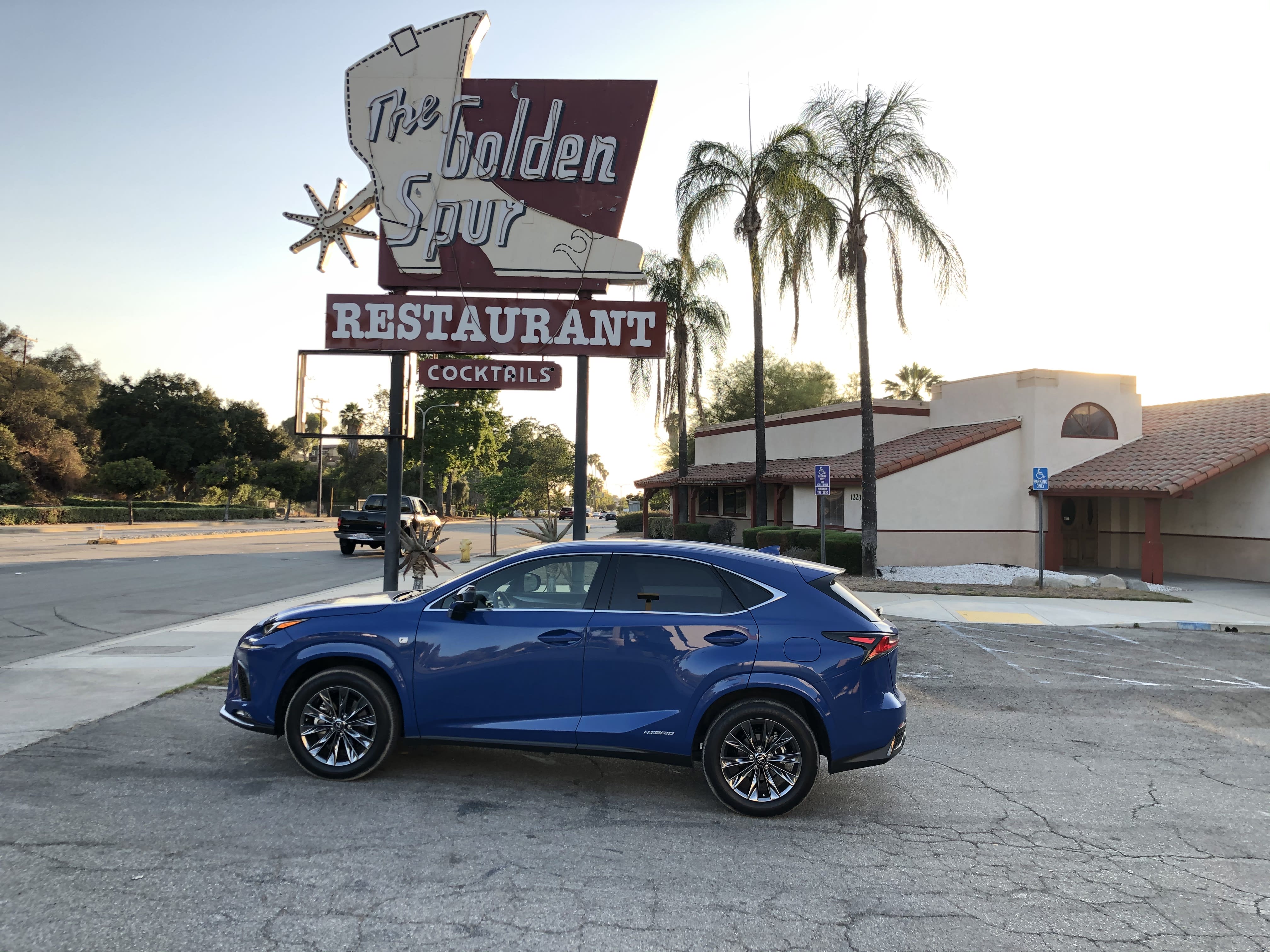 A Lexus NX 300h F Sport parked on a deserted parking lot in SoCal, under a vintage sign.