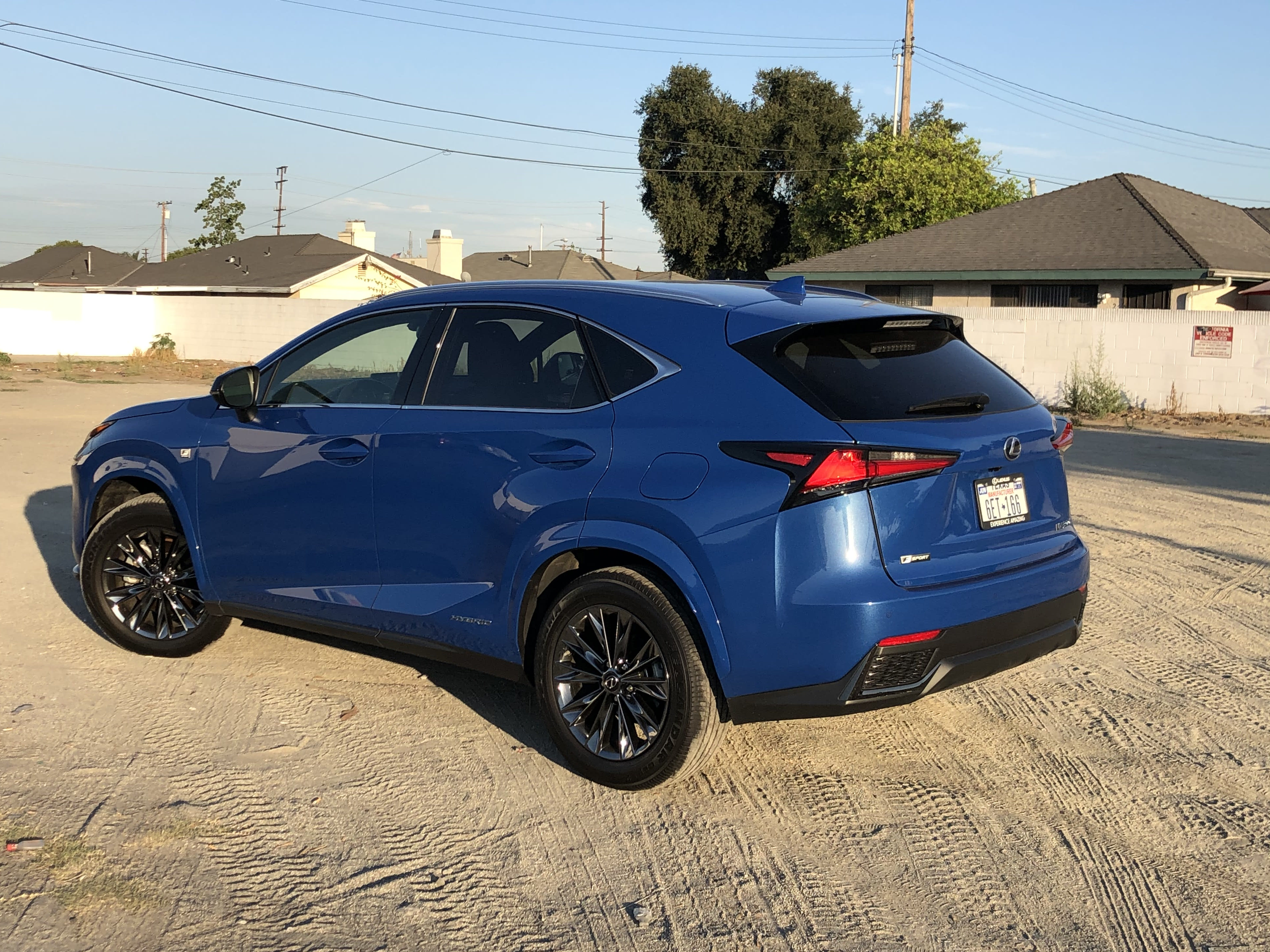 the rear and left exterior of a blue Lexus NX 300h F Sport parked on a sandy deserted lot.