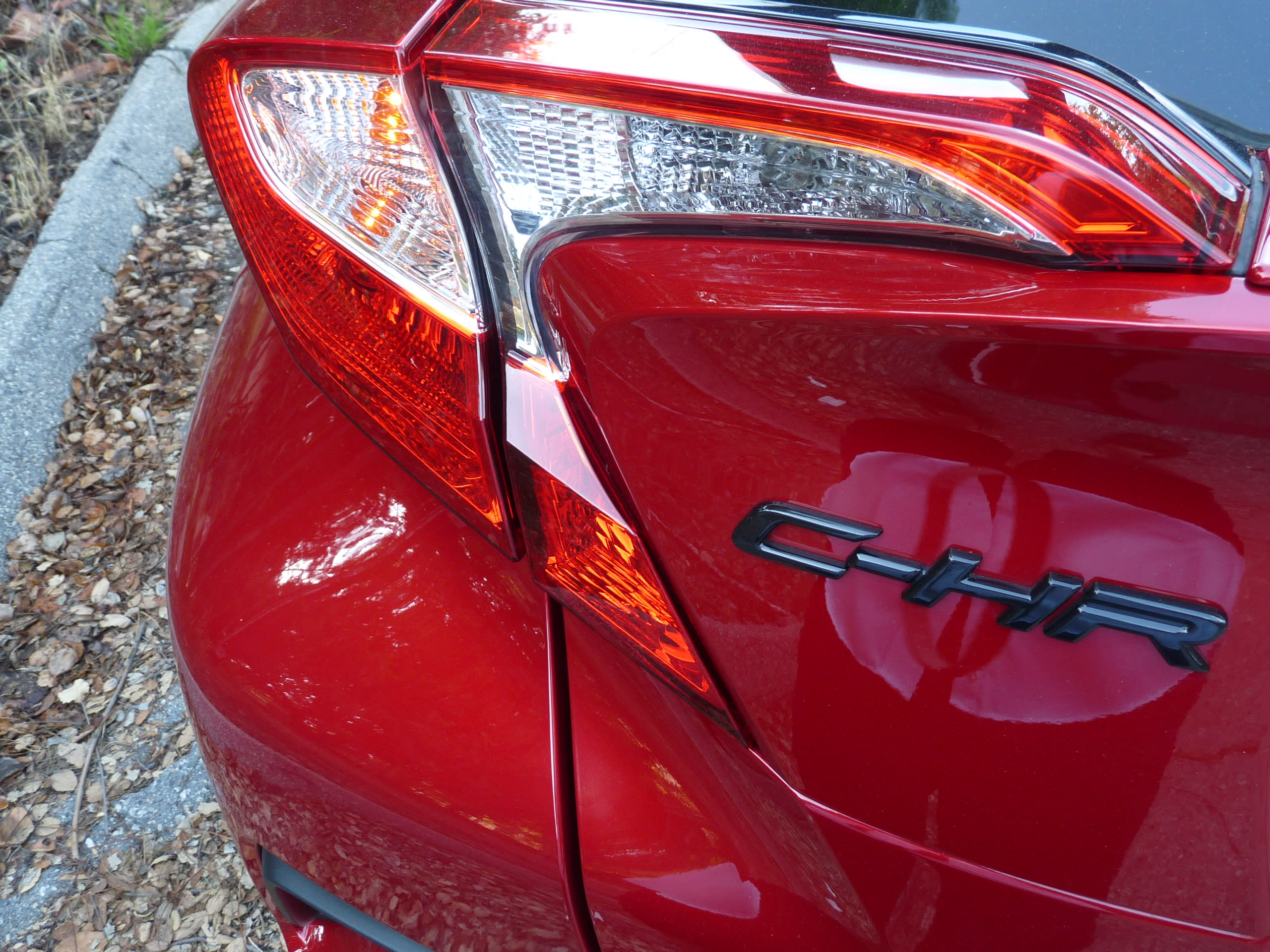 left rear tail-lights of the red Toyota CH-R with sharp design angles and a dark "CH-R"-logo