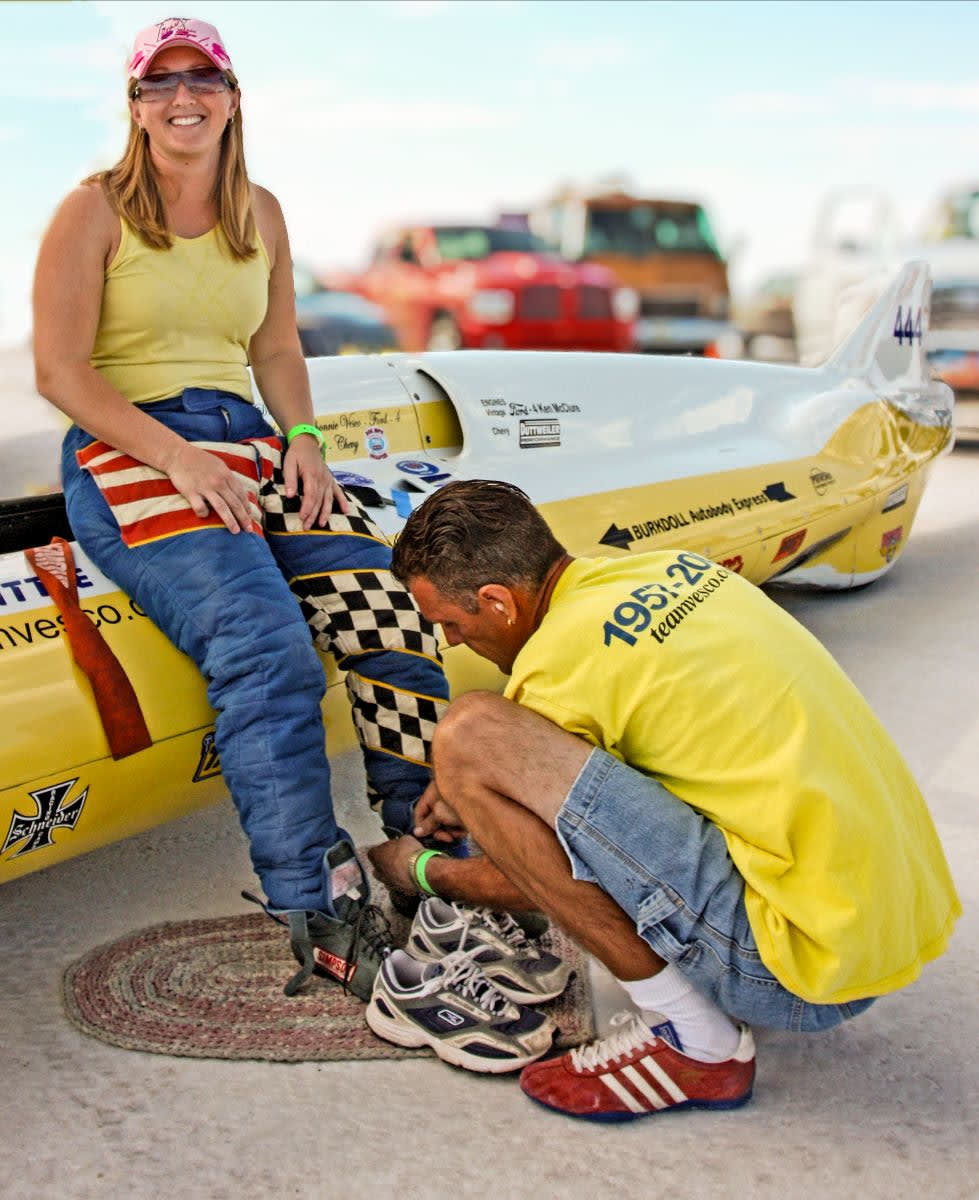 Rhonnie Vesco getting her shoes tied by a team member before getting into the family streamliner at the Bonneville Salt Flats.