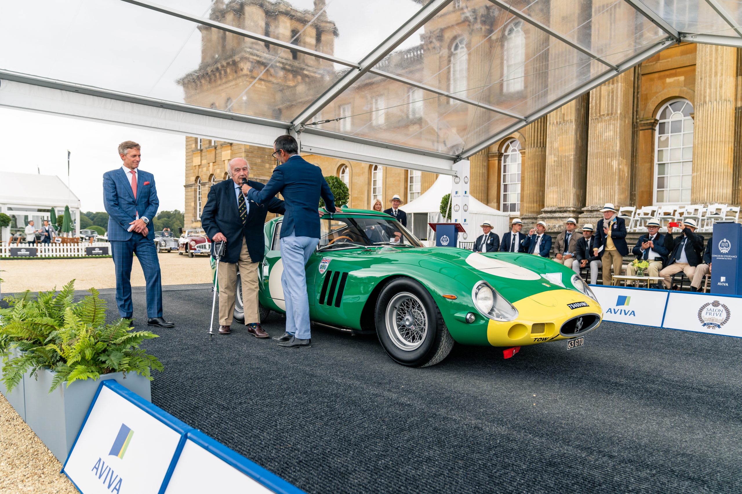 classic green Ferrari GTO race car with men in suits standing around it.