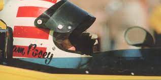 Sam Posey wearing a helmet, sitting in a race car.