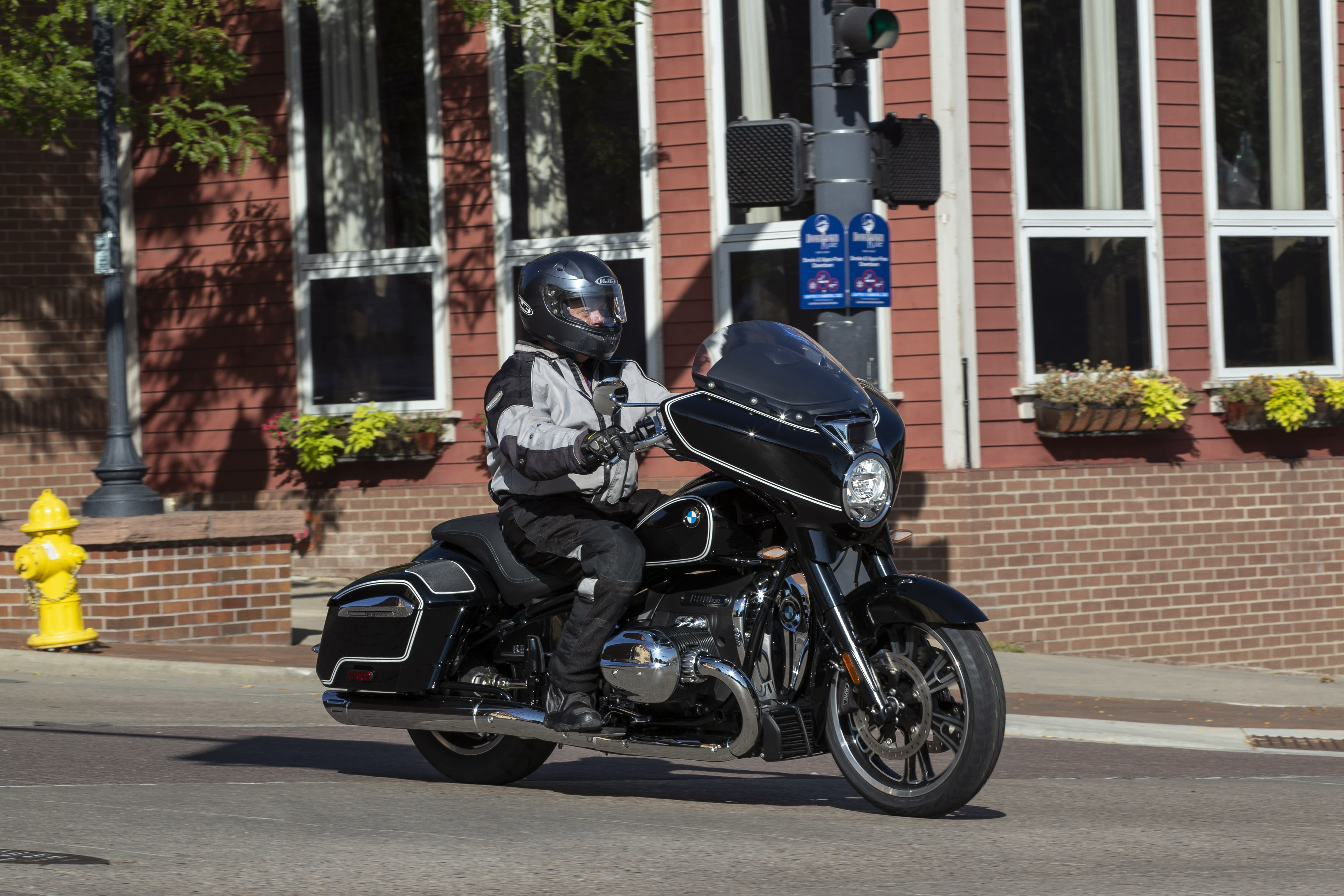 A BMW R 18 B cruising through a city, with a brick house in the background