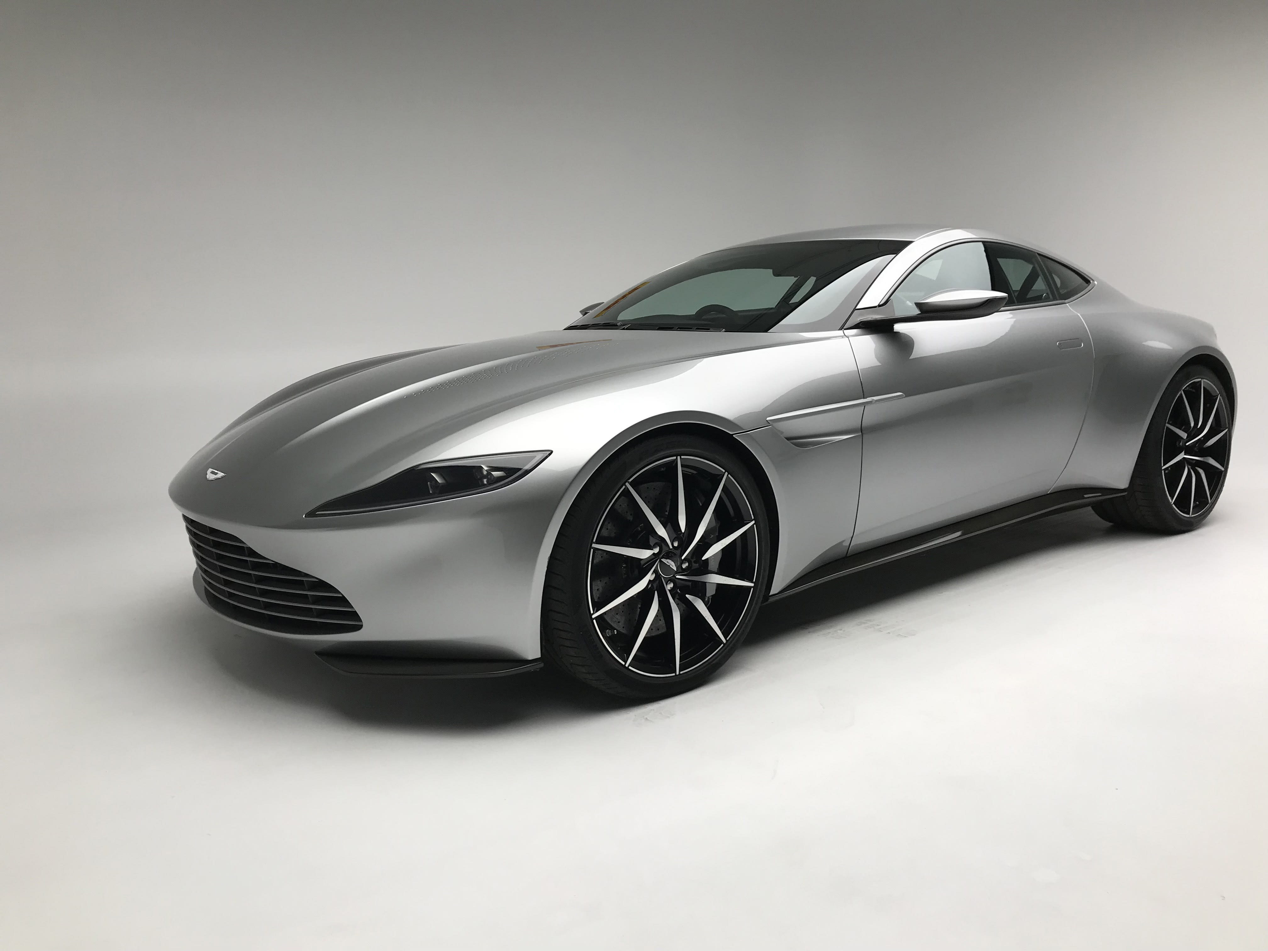 A silver Aston Martin DB10 with massive rims, photographed in a studio