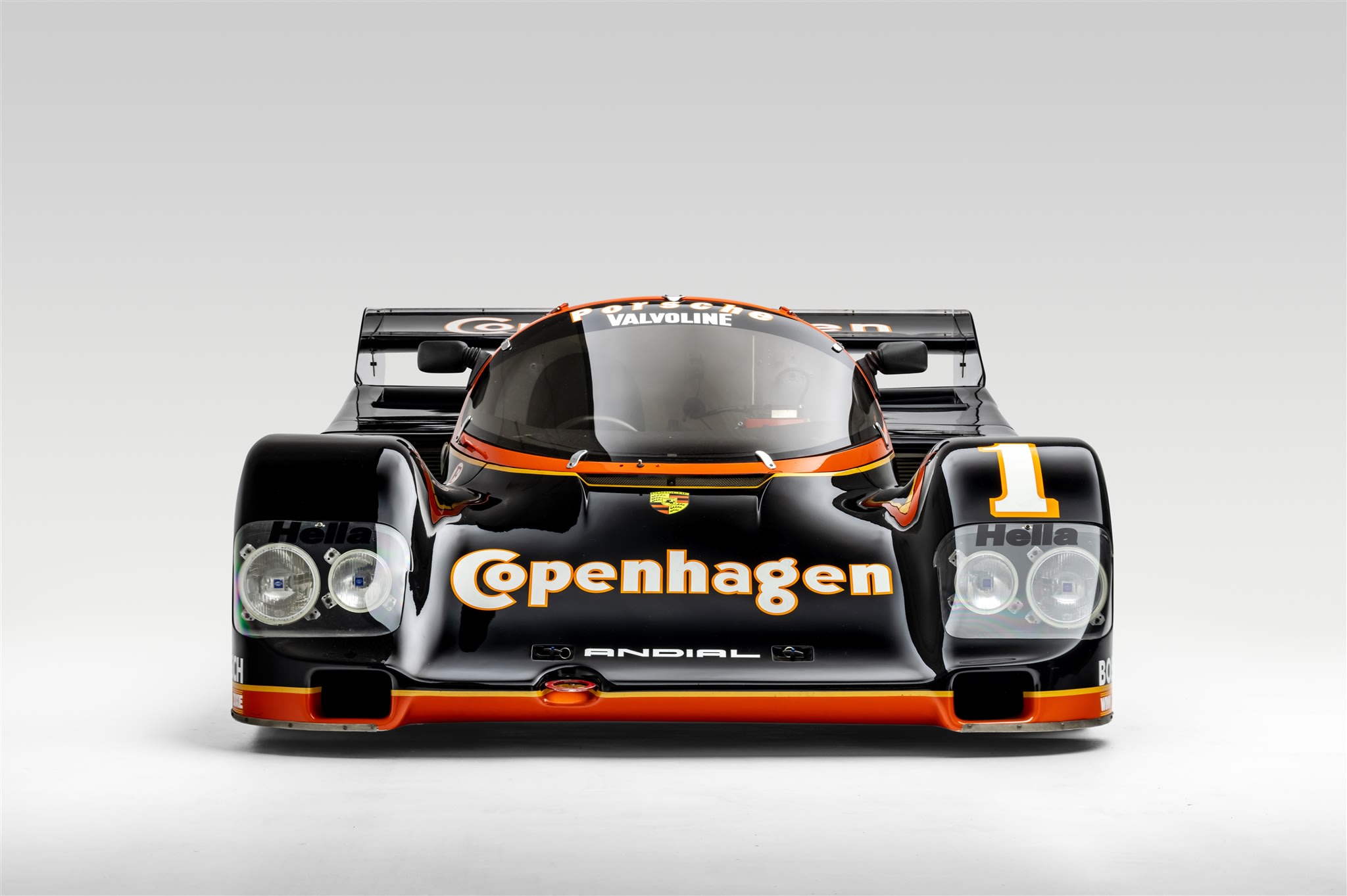 A black Porsche 962 with orange details, sponsored by Copenhagen