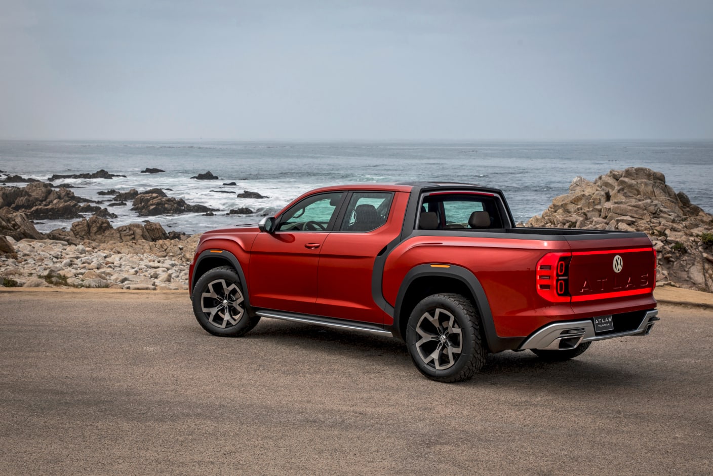 a red Volkswagen Atlan Tanoak driving on the shores of what could be Southern California.