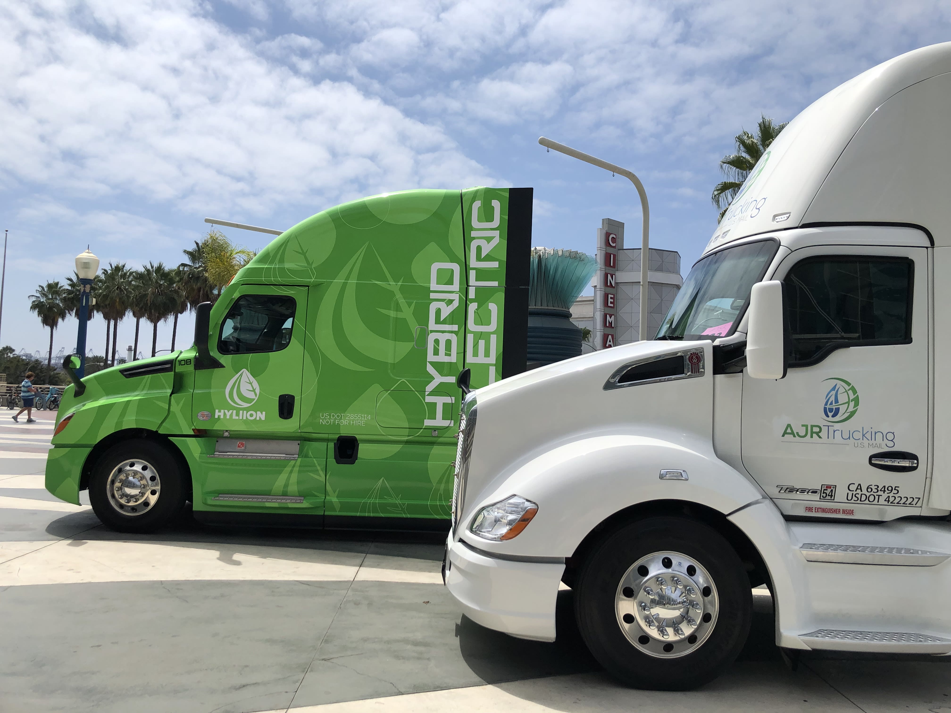 two trucks at a stoplight, one of them is labeled as a hybrid electric truck.