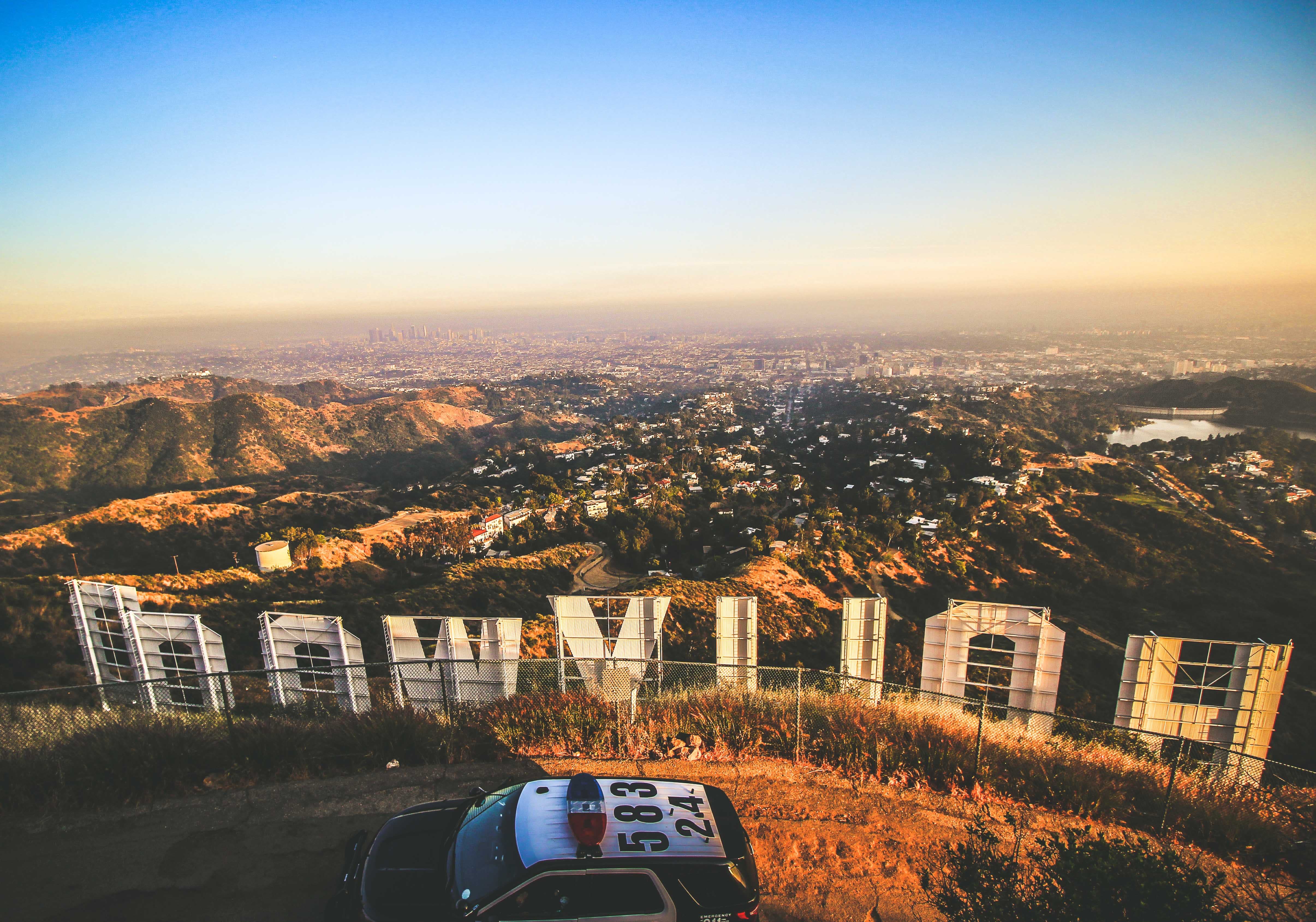 a view of Los Angeles from behind the Hollywood sign, with a police car in the foreground.