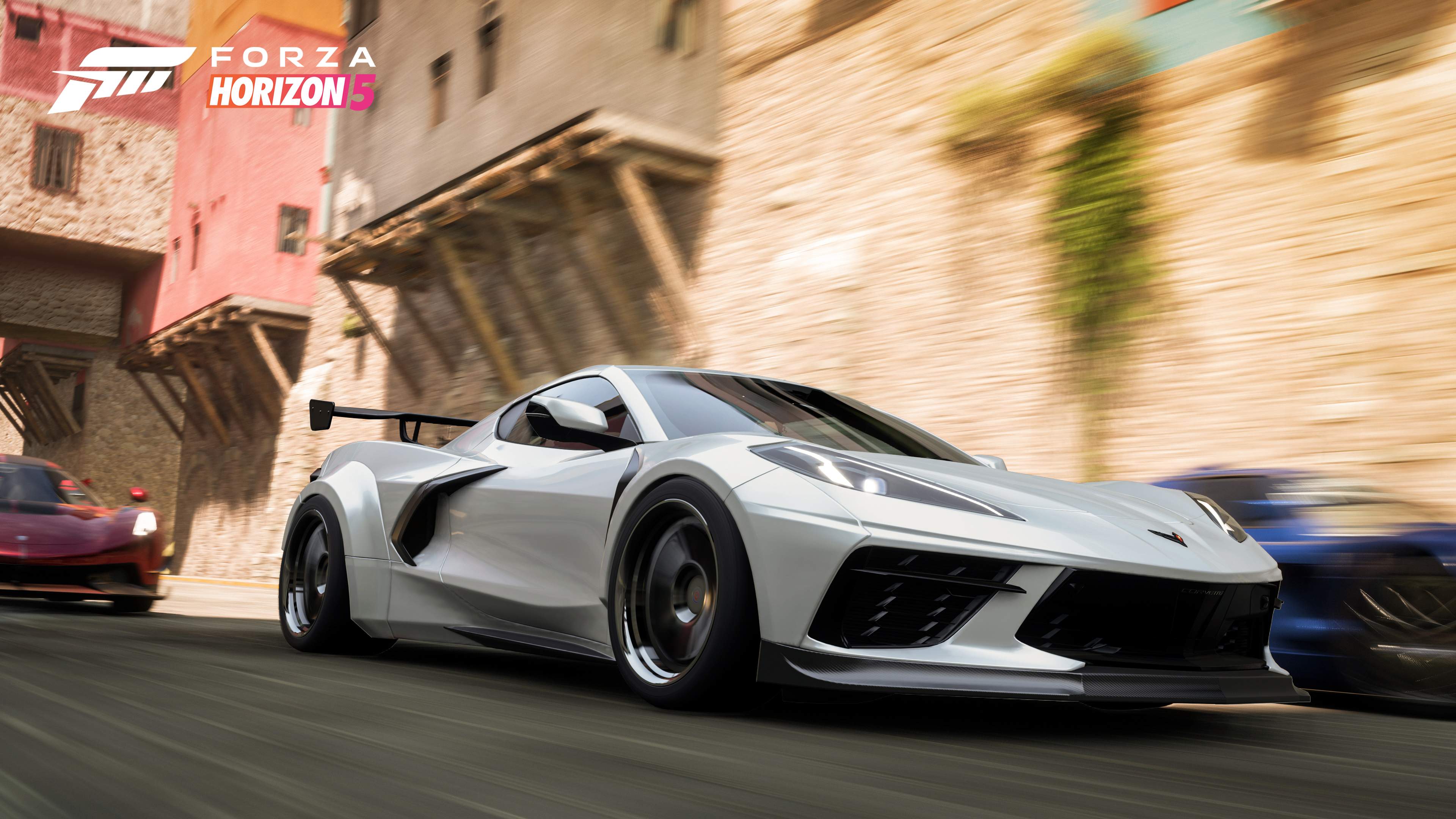 image from the Forza Horizon 5 video game with a silver white Corvette C8 in the foreground, racing down city streets with other exclusive cars in tight pursuit.