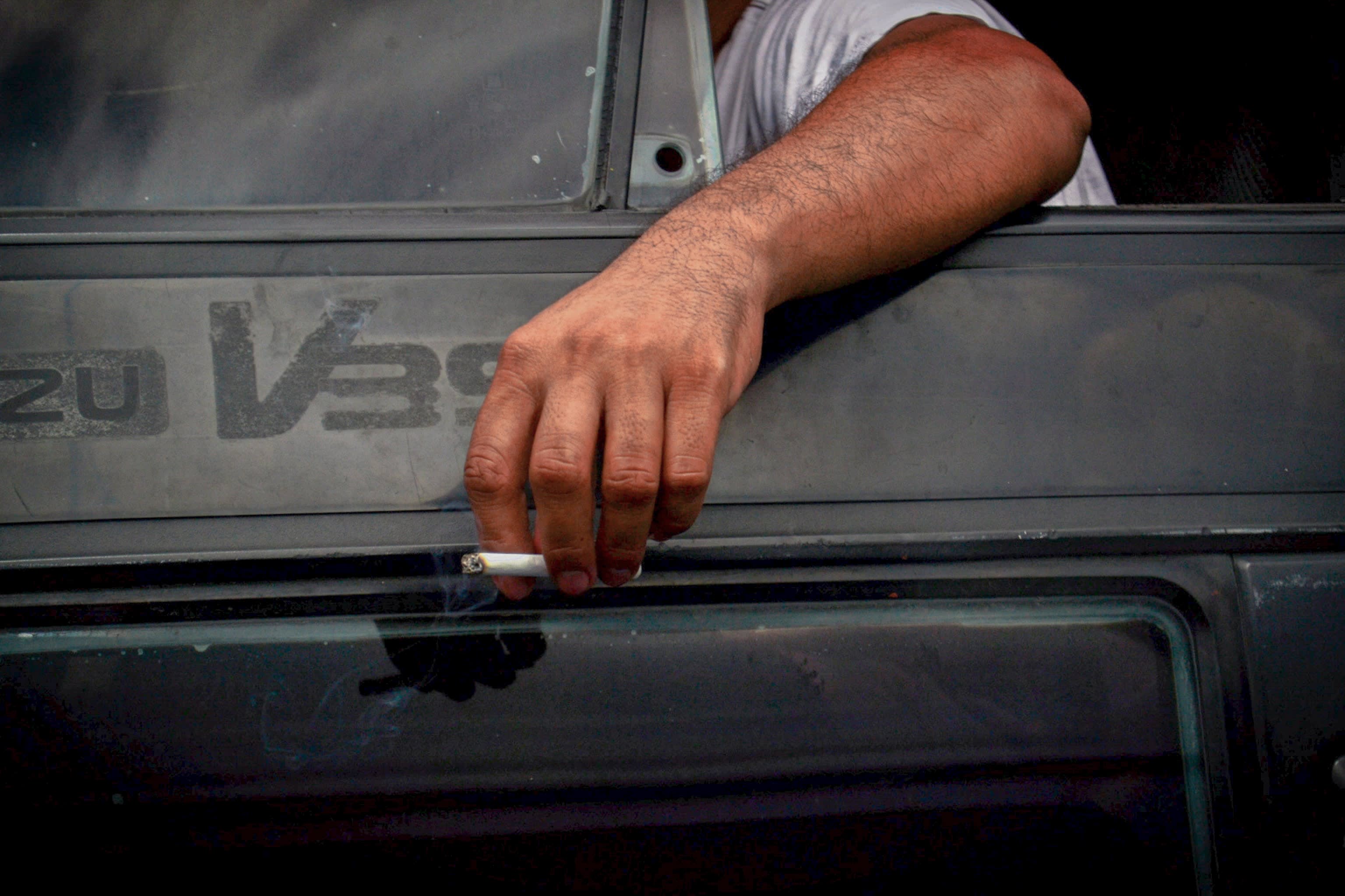 man holding a cigarette outside his car door, through the window.