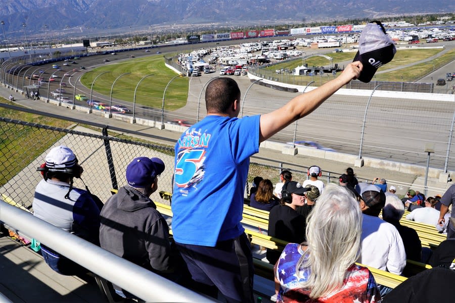 NASCAR fan in the stands waving hit hat as the racers pass by