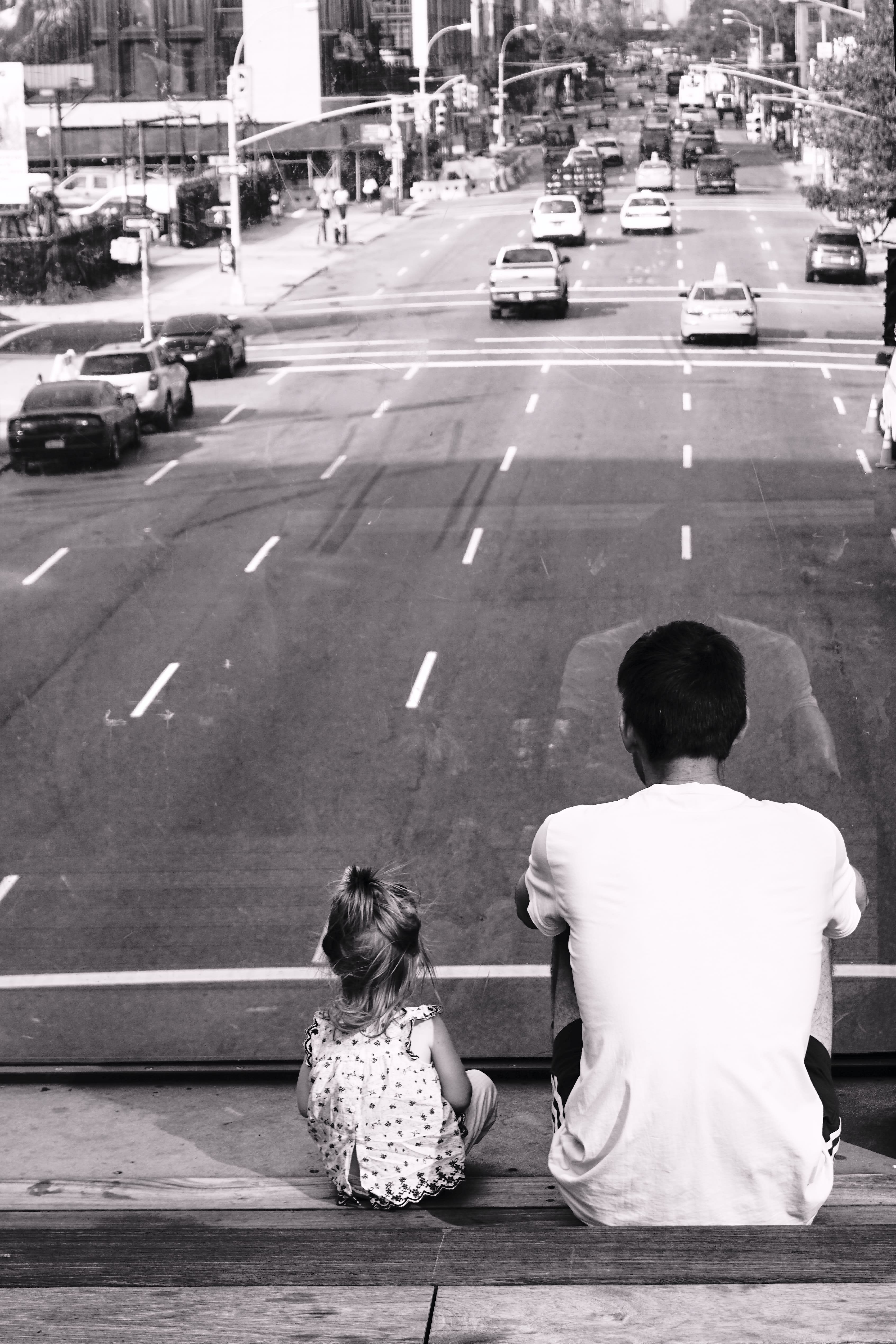 father and daughter sitting on an overpass, looking at the cars below.
