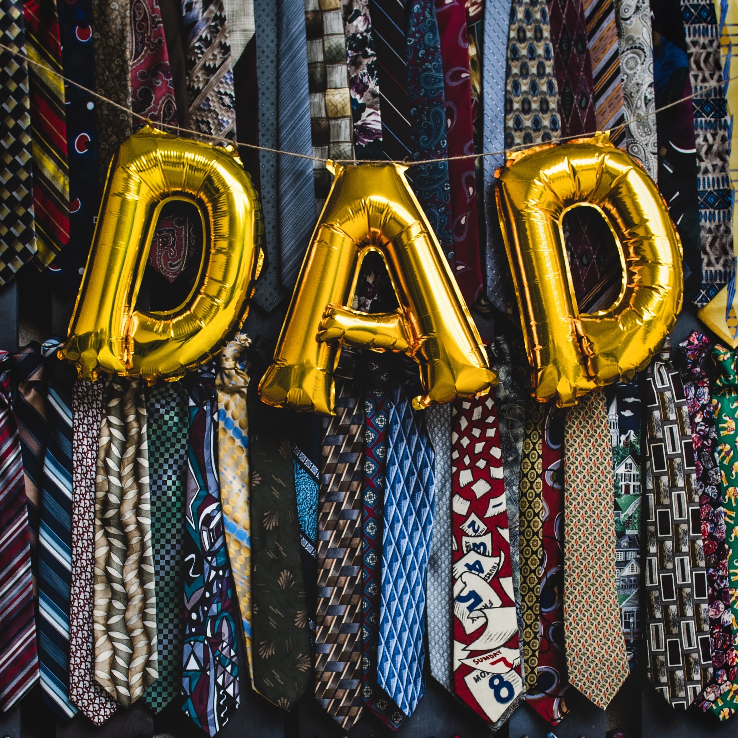 a collection of ties, with big ballons hanging in the foreground, spelling out DAD.